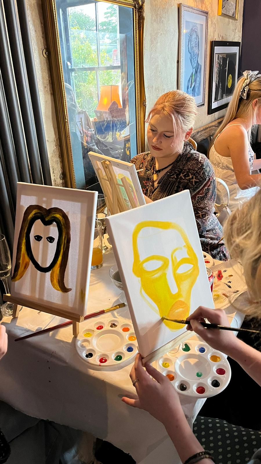 A group of women engaged in painting together at a table, surrounded by various colors and art supplies.